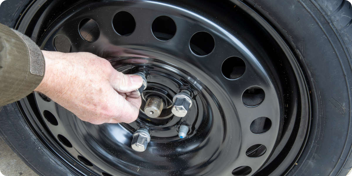 Eine Hand hält eine lockere Radmutter an einer schwarzen Stahlfelge in der Hand.