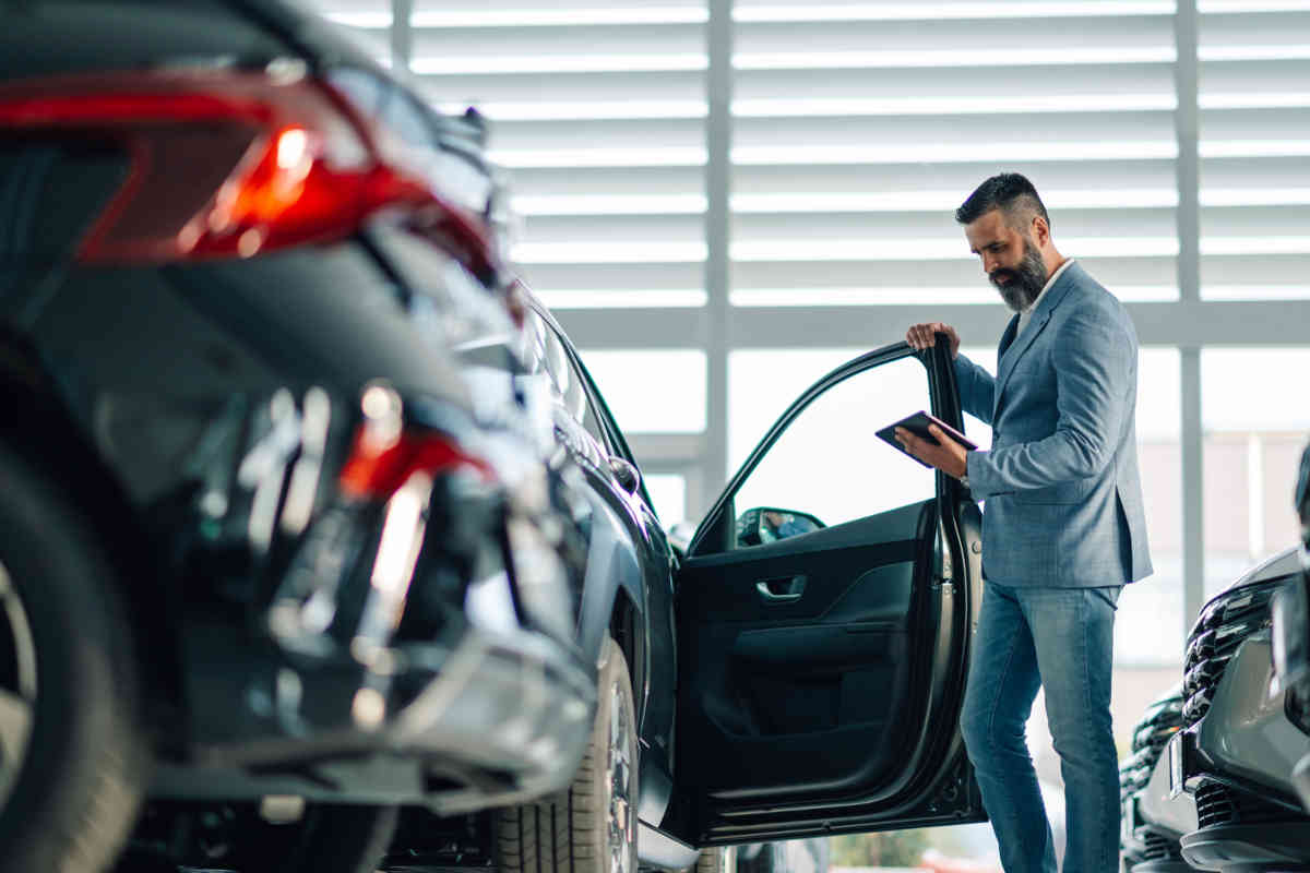 A man stands next to a new car and looks at his smartphone.